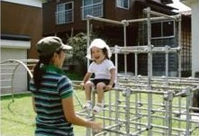ジャングルジムに笑顔で座る子供とそれを見守る女性の写真