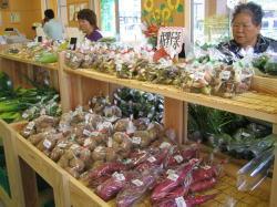 たくさんの袋に詰められた野菜が棚に置かれ、それを見ている年配の女性の写真