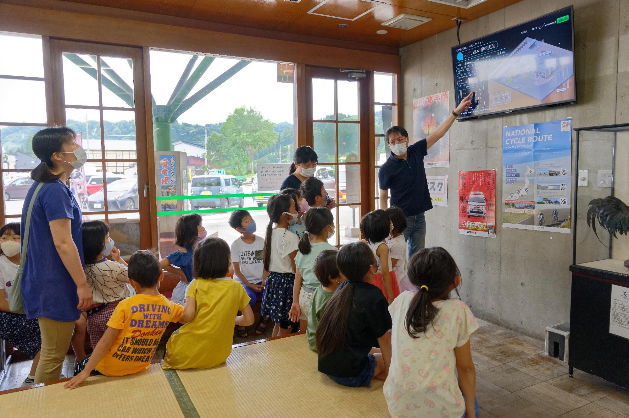 子どもたちにモニターを用いて設備の説明をする様子
