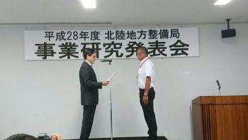 横断幕の前で、地方整備部長が係長を表彰している、事業研究発表会表彰式の写真