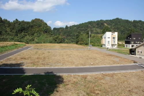 芝生が広がる土地の奥に山林が見える写真