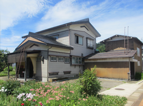 色とりどりの花が咲く花壇が近くにある白い2階建て一軒家の写真