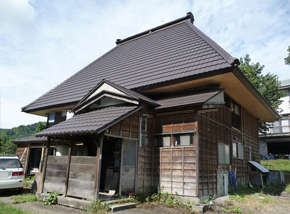 屋根が四方に向けて傾きが急な濃い茶色の2階建て一軒家の写真
