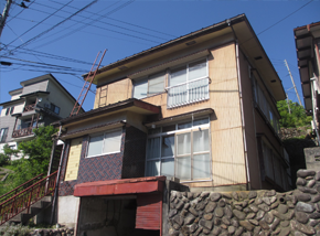 石垣の上にある薄茶色の2階建て一軒家の写真