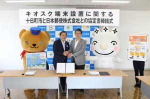 協定書締結式にて握手を交わす市長と青木代表の写真