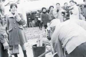 臼と杵でついたもちを食べながら雪まつりを楽しんでいる女性のモノクロ写真