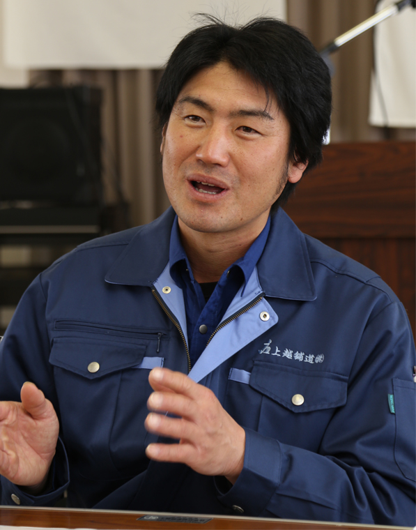 作業中を着た男性が手ぶりを交え話をしている