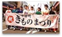 晴れ着を着た8人の女性が「十日町きものまつり」と書かれた垂れ幕を持って歩いている処の写真