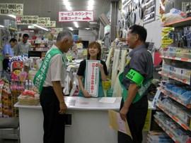 十日町市内のお店を該当巡回パトロールしている緑色のたすきと腕章を付けた青少年育成委員の男性2人と渡された啓発ポスターを両手に持った従業員の女性の写真