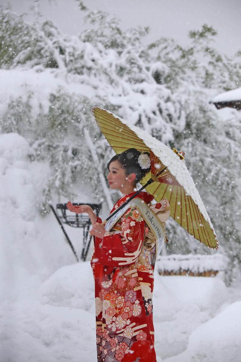 きものを着ている女性が雪が降る中傘をさしている様子