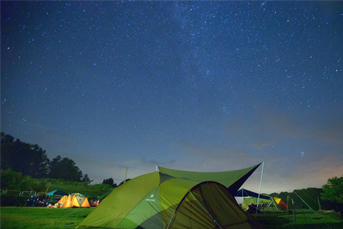 キャンプ場にテントが張られていて、空には満点の星空が広がっている景色