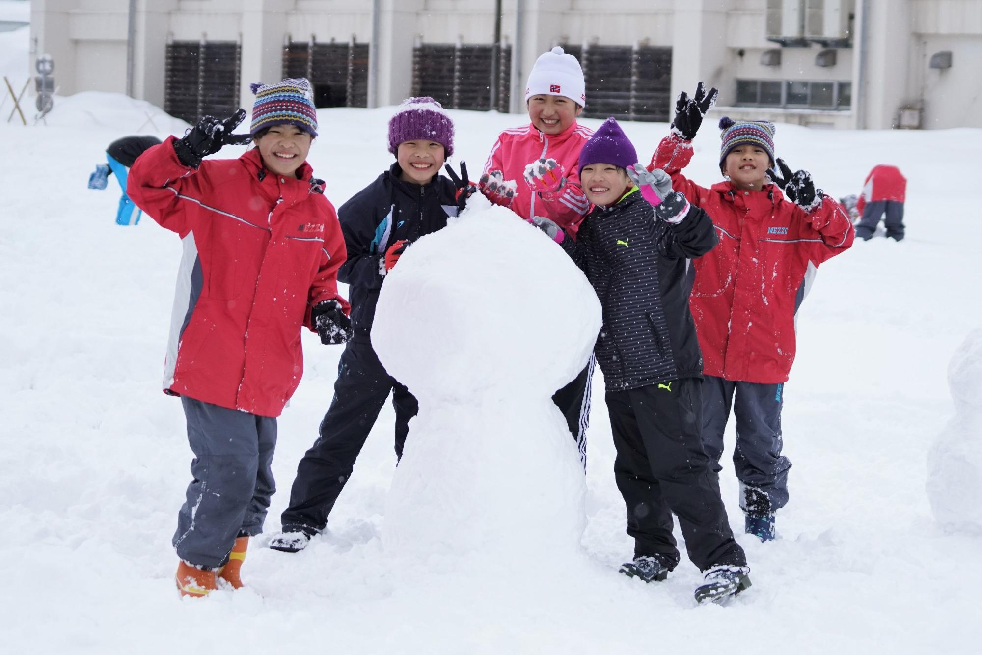 雪だるまを作り笑顔でピースをしている5人の小学生