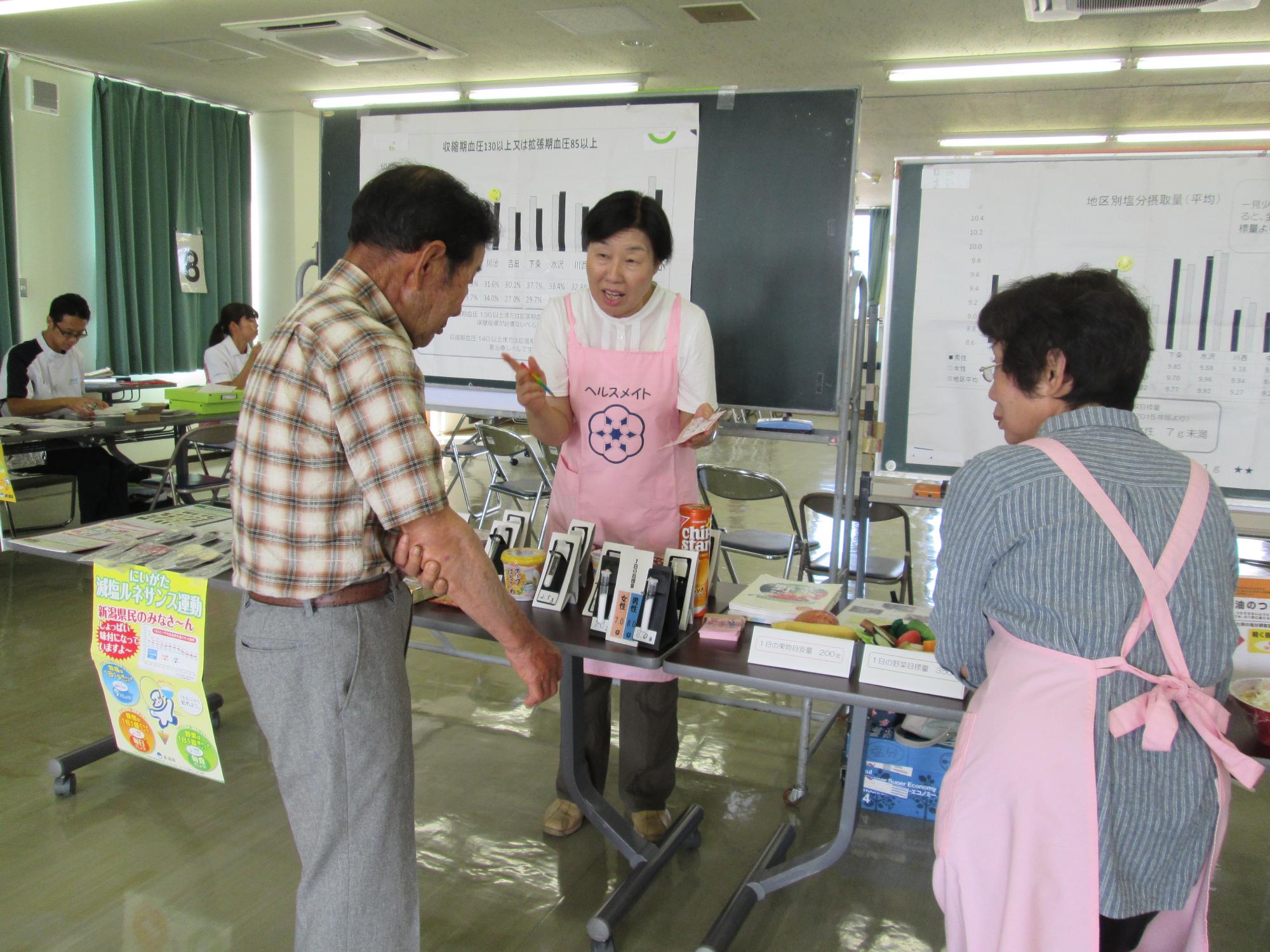 住民健診の会場で、食生活改善推進員が受診者にバランス食などの啓発をしている写真