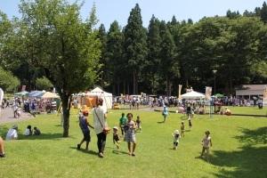 木々に囲まれた公園で家族連れなどが遊んでいる写真