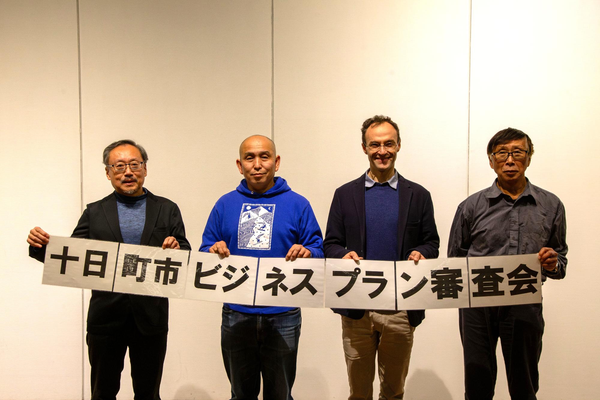「十日町市ビジネスプラン審査会」の看板を持って集合写真を撮るプレゼン参加者一同の写真