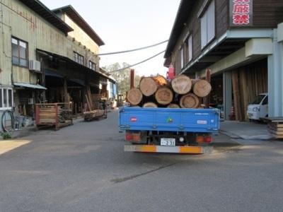青いトラックに多くの丸太が積まれ、製材工場に到着した処の写真