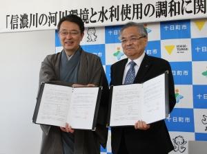 自治体のロゴが描かれた壁紙を背に、握手をする関口市長と冨田社長の写真