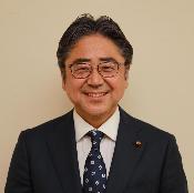 眼鏡をかけ、スーツを着て微笑んでいる富井高志議員の写真