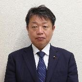 スーツを着て微笑んでいる福崎哲也議員の写真