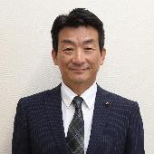 スーツを着て微笑んでいる村山達也議員の写真