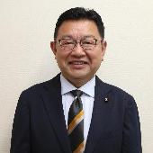 眼鏡をかけ、スーツを着て微笑んでいる根津年夫議員の写真