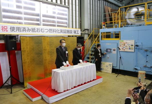 テーブルの上に置かれたスイッチ押下する関口市長（左）と、十日町市義市議会議長・鈴木一郎の写真