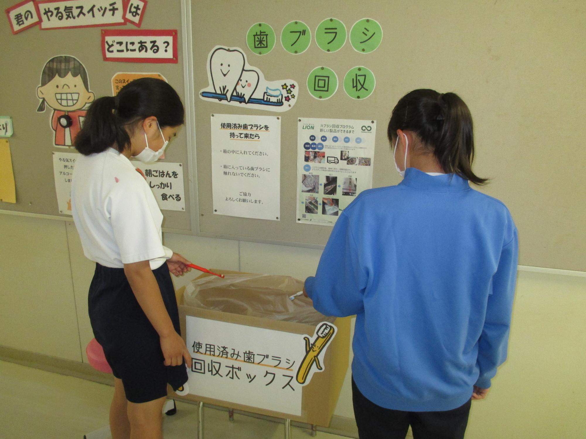 回収ボックスに使用済み歯ブラシを寄付する2人の女子中学生