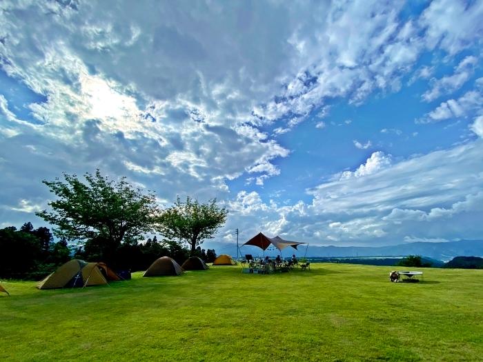 広々とした青空のもと芝生が映えるキャンプ場の写真