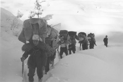 大きな荷物を背負って、列をなして雪原を進む逓送隊の写真