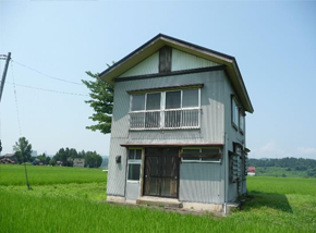 田んぼの中心にある白い2階建て一軒家の写真