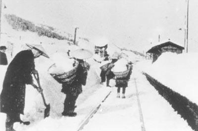 スコップと籠を使った人海戦術でホームの除雪作業を行う人々の写真