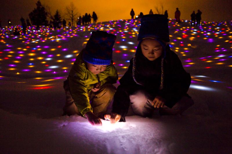 タイトル「Gift for Frozen Village」と名付けられた窪んだ雪の中に色とりどりの明かりを置いている2人の児童の写真