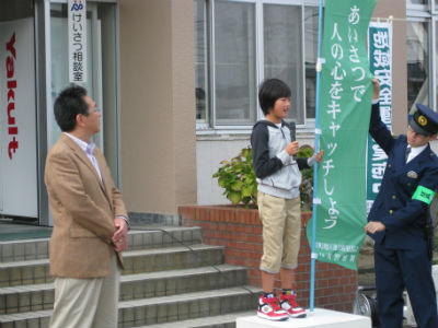 小学生が標語が書かれた旗を持って台に上がっている。