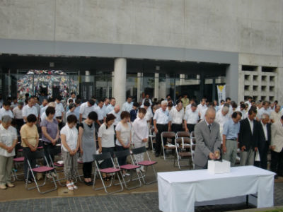 屋外でたくさんの人々が黙祷をささげている。