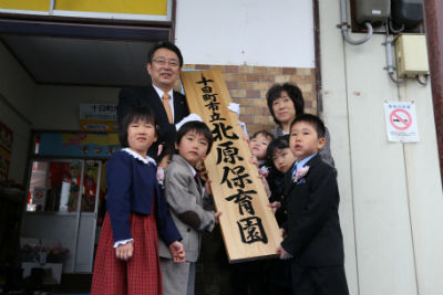 関口市長と子供たちが保育園の看板を持ち上げている。
