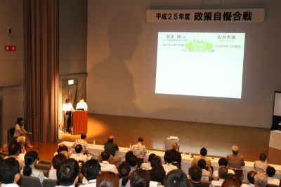 参加者がステージ上でスライドを用いて発表している。