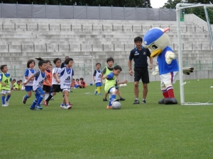 子供たちがマスコットキャラクターと一緒にサッカーをしている。