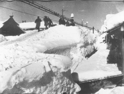 電線まで積み上がった雪を除雪している人たちの写真