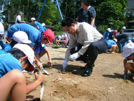 校庭で、関口市長が多くの児童たちと一緒に苗を植えている。