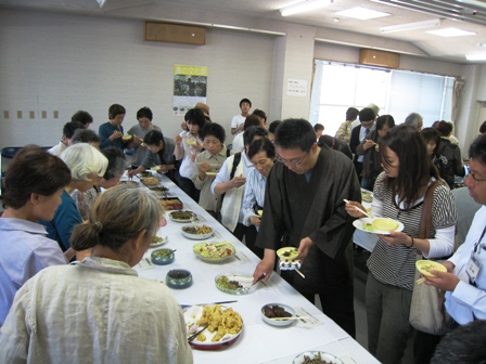 テーブルに並べられた数々の料理を関口市長と参加者たちが立食している。