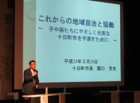 関口市長がステージ上でスライドを用いて発表している。