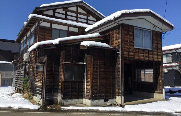 屋根に雪が被った濃褐色の木造式一軒家の写真