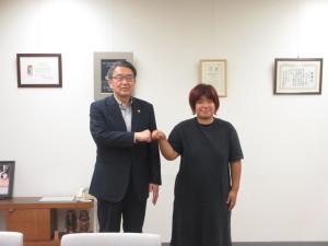 報告会にて、片桐女史とフィストバンプして記念撮影に応じる市長の写真