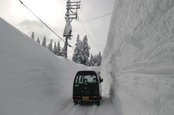 左右とも雪の壁となっている車道を走る車の写真