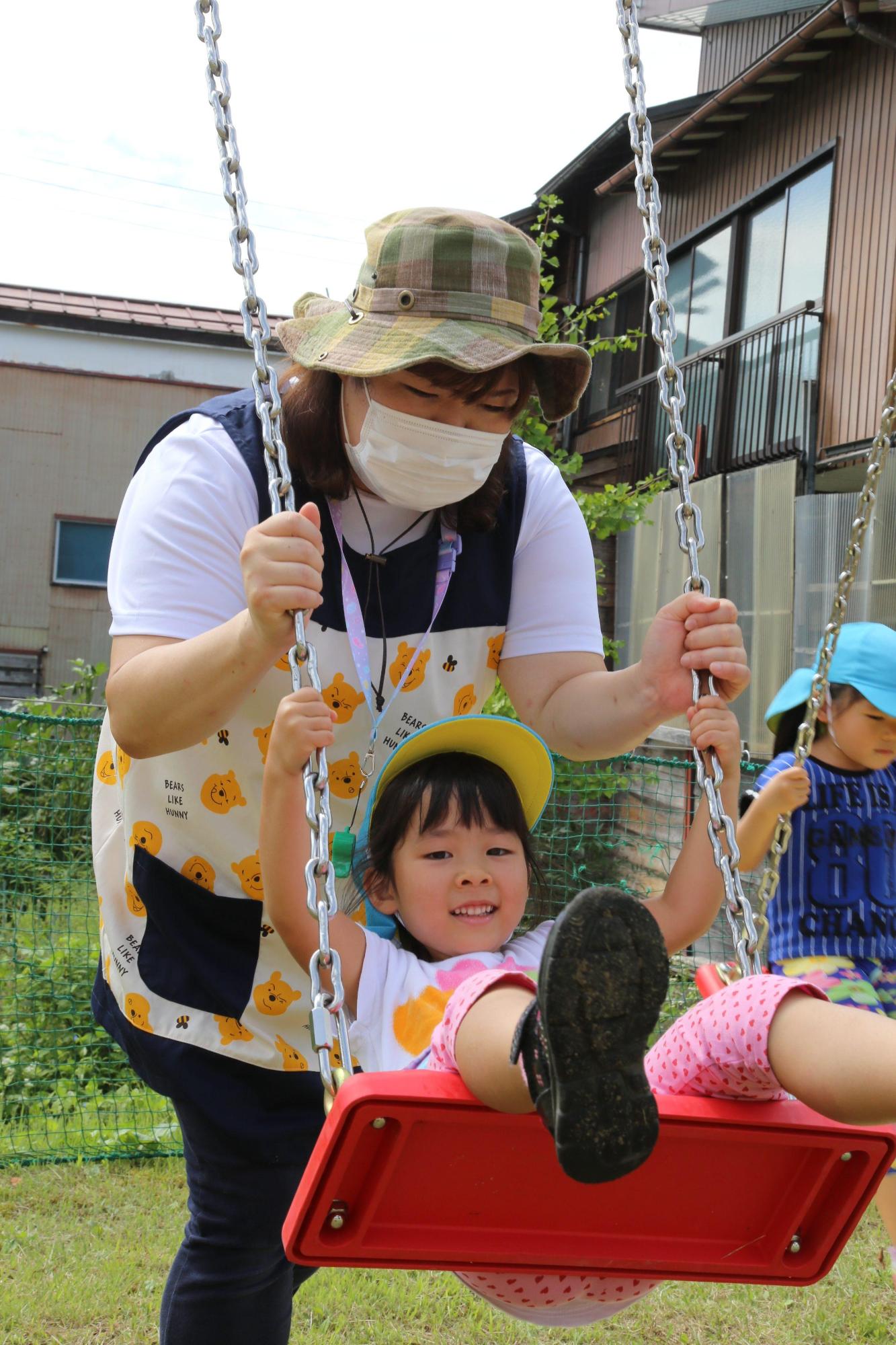 ブランコに乗る子供とブランコを押す女性の写真