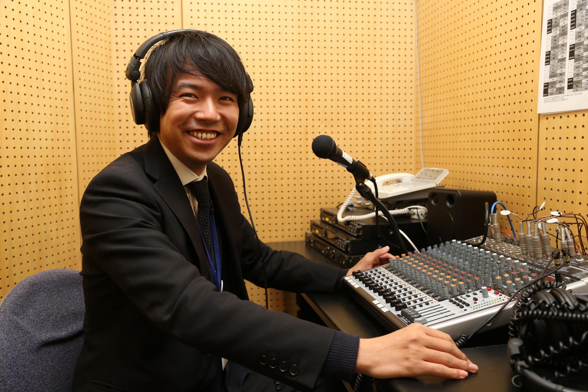 ラジオ局で、株式会社エフエムとおかまちに勤務する樋口智史さんがヘッドホンを付け、笑顔で写っている写真