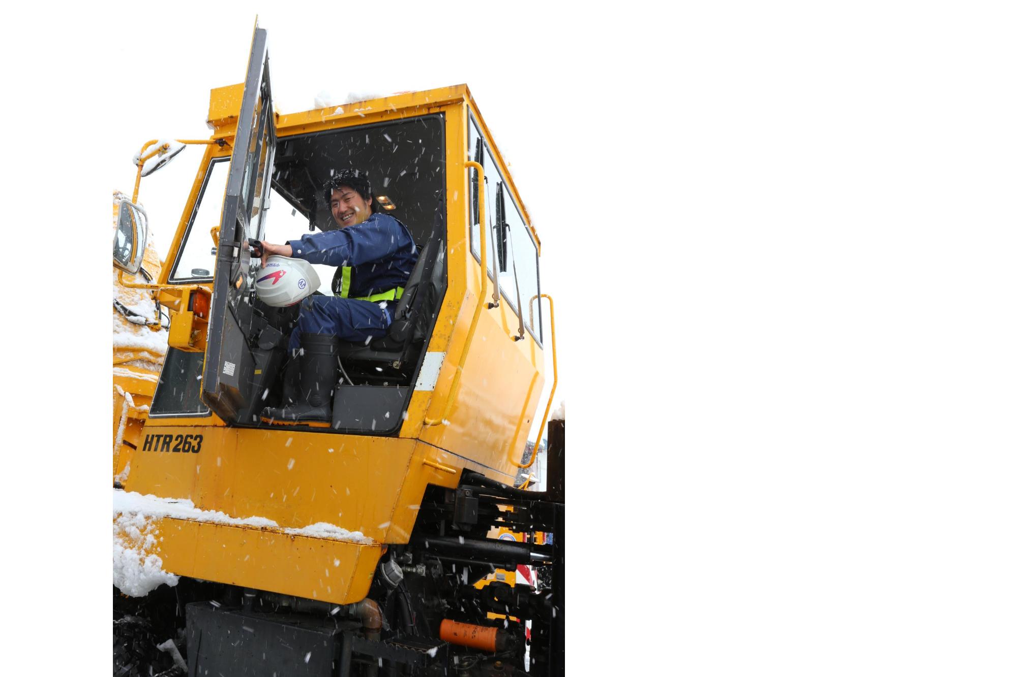 雪の降る中除雪車に乗り込む笑顔の男性