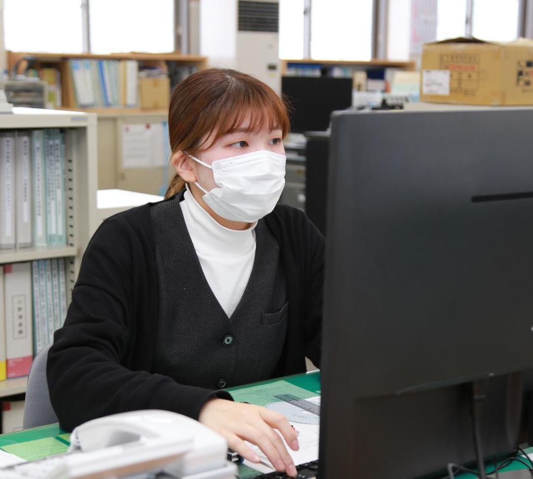 マスクをした女性がパソコンで作業をしている