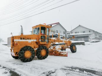 黄色い除雪車が雪道の雪を除雪している様子の写真
