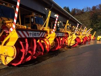5台の除雪車が駐車場で並んでいる様子の写真